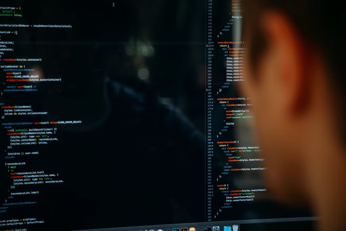 A imagem mostra uma pessoa observando atentamente uma tela de computador com código-fonte — provavelmente relacionado a desenvolvimento de software. O código parece estar escrito em JavaScript (ou JSX), comum em aplicações web. Essa cena sugere um ambiente de desenvolvimento técnico voltado à criação de soluções digitais, como ferramentas de análise de crédito automatizadas.