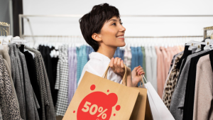 A imagem mostra uma mulher de cabelo curto e escuro a sorrir enquanto faz compras numa loja de vestuário.
