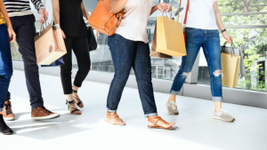 A imagem mostra um grupo de pessoas caminhando lado a lado em um ambiente interno, possivelmente um shopping ou centro comercial.